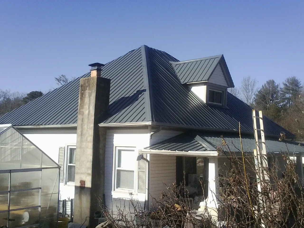 Dark blue standing seam metal roof on a white farmhouse with dormer — Slate & Tile Roof Repair by Roofing Brothers in Imlay