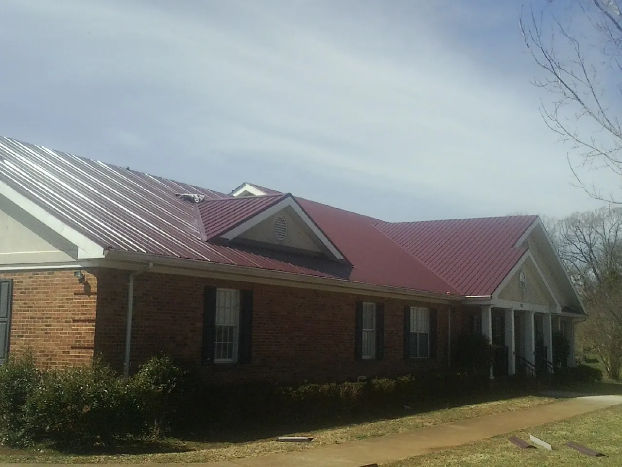 Red metal roof with gabled entries on a long brick building, from a Hail Damage Roof Repair job in Imlay