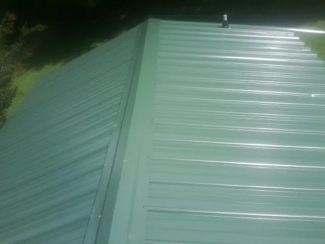 New green metal panels meeting at the ridge of a roof — Flat Roof Repair work by our crew in Imlay