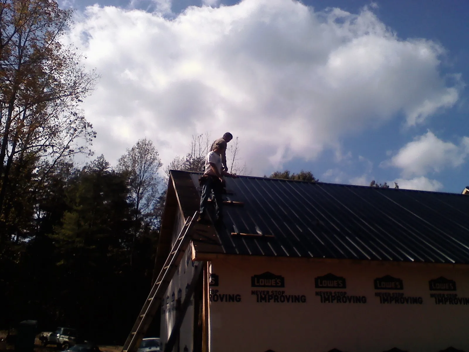 Roofer fastening dark metal panels high against a cloudy sky, from a Roof Inspection job in Imlay
