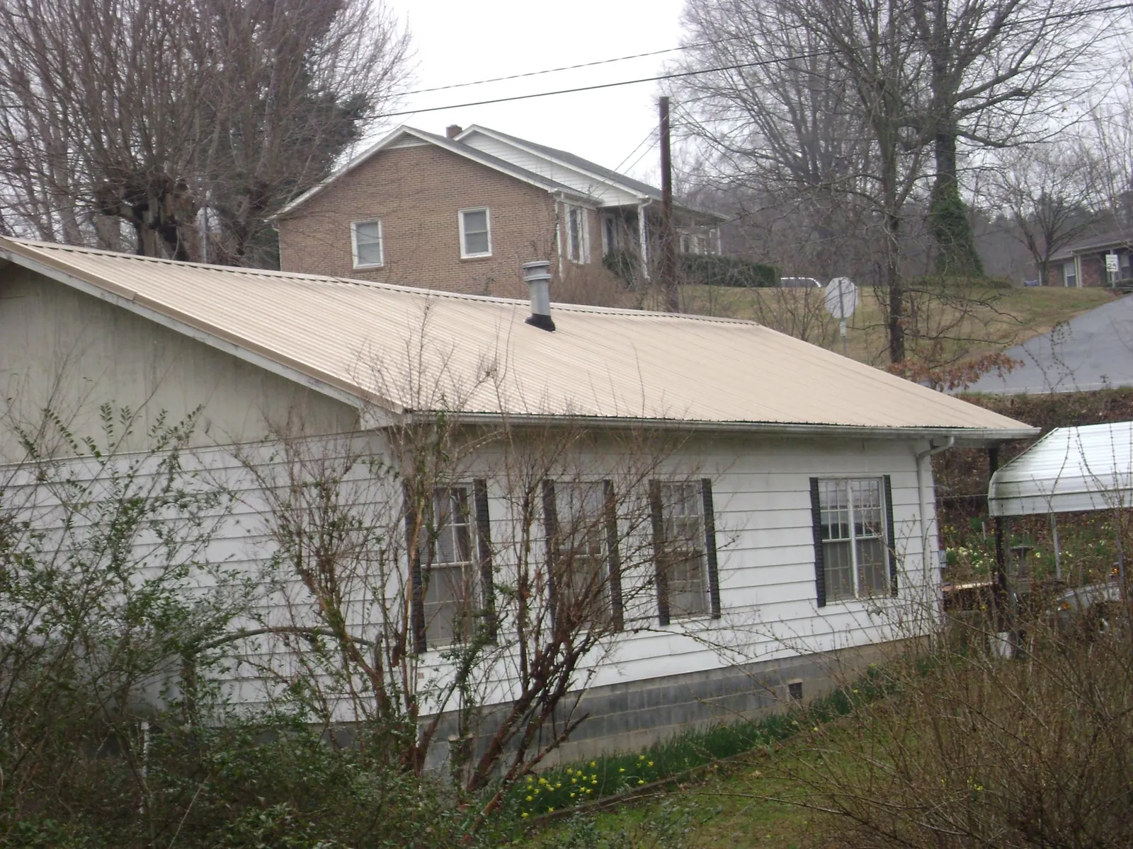 Tan metal roof on a white sided house set into a hillside — Commercial Roofing by Roofing Brothers in Imlay
